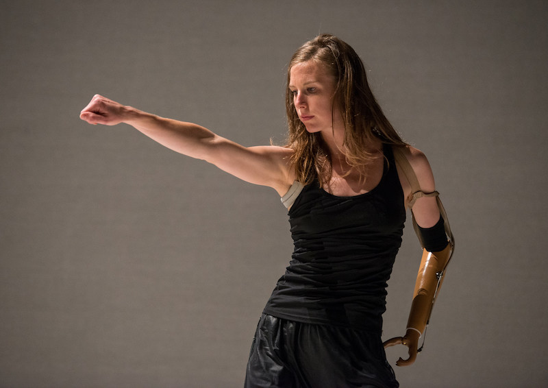 A women punches her right arm out. Her gaze is down.